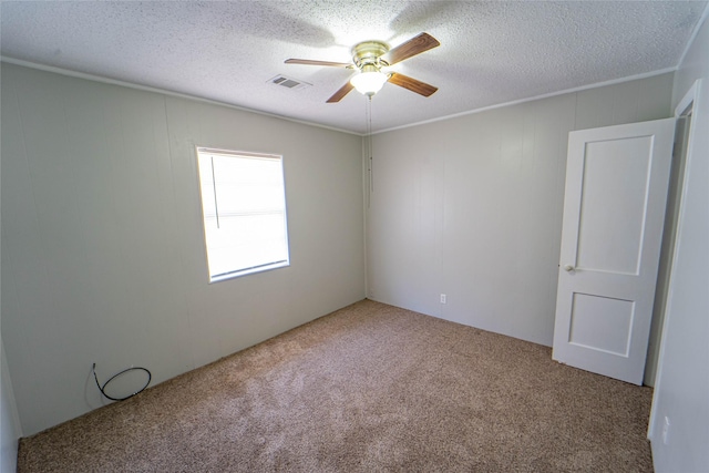 carpeted empty room with a textured ceiling, ceiling fan, visible vents, and crown molding