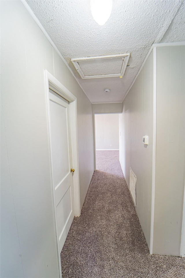 corridor with carpet floors, attic access, visible vents, and a textured ceiling