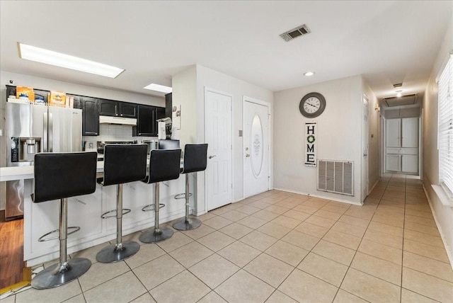 kitchen with visible vents, a kitchen breakfast bar, dark cabinets, and light tile patterned flooring