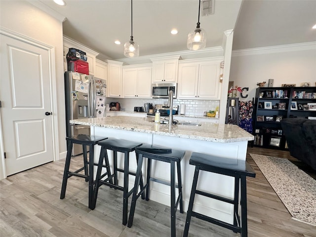 kitchen featuring pendant lighting, stainless steel appliances, light stone counters, and white cabinets