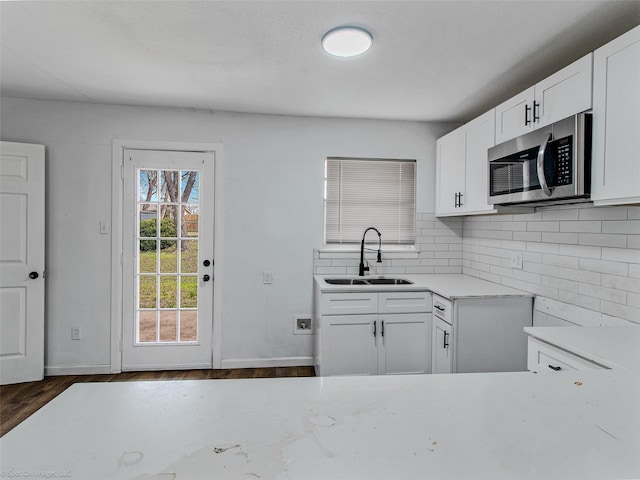 kitchen featuring a sink, stainless steel microwave, backsplash, white cabinets, and dark wood-style flooring