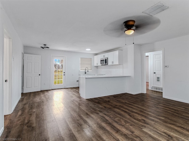 unfurnished living room with visible vents, baseboards, dark wood-style floors, and a ceiling fan