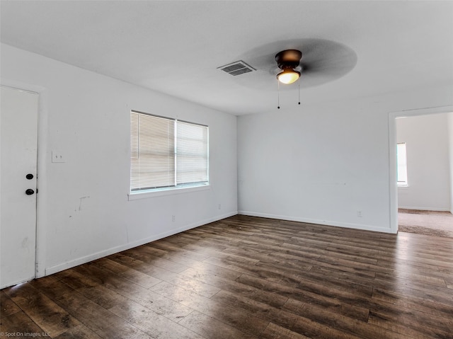 empty room featuring ceiling fan, visible vents, baseboards, and dark wood finished floors