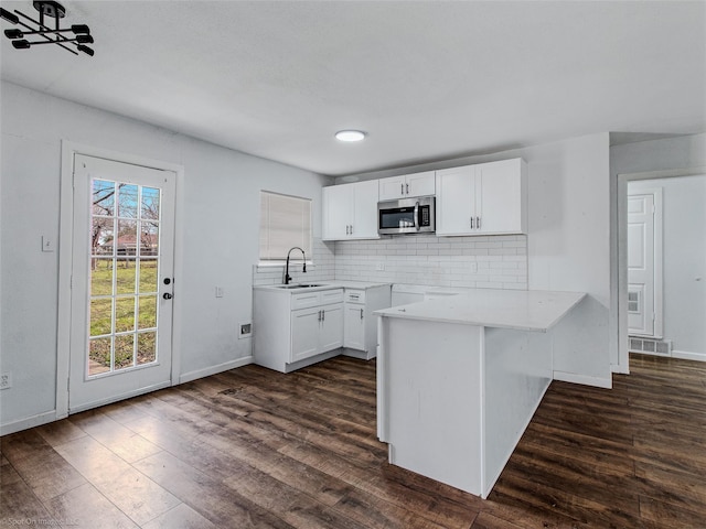 kitchen with dark wood finished floors, a sink, decorative backsplash, white cabinetry, and stainless steel microwave