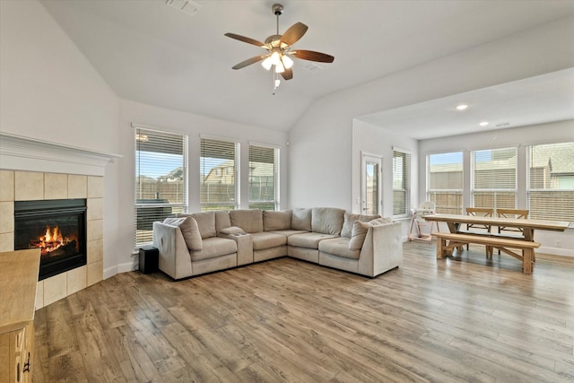 living area with visible vents, a tiled fireplace, lofted ceiling, ceiling fan, and wood finished floors