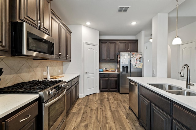 kitchen with stainless steel appliances, a sink, hanging light fixtures, and dark brown cabinetry