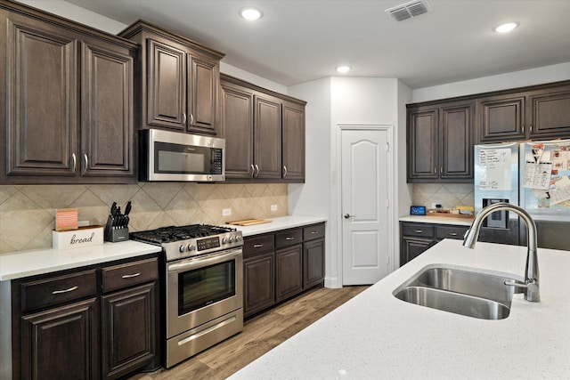 kitchen with light wood finished floors, visible vents, appliances with stainless steel finishes, dark brown cabinetry, and a sink