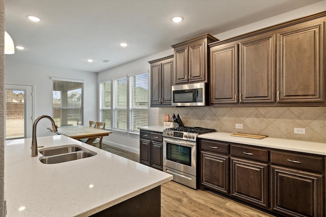 kitchen featuring a sink, light wood-style floors, dark brown cabinets, appliances with stainless steel finishes, and tasteful backsplash