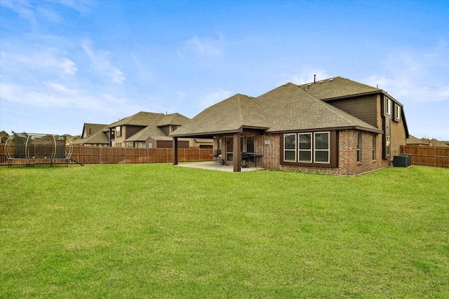 back of property with a fenced backyard, a trampoline, a yard, a patio area, and brick siding