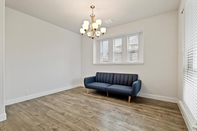 living area featuring a notable chandelier, visible vents, baseboards, and wood finished floors