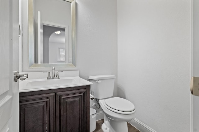 half bathroom featuring toilet, wood finished floors, vanity, and baseboards