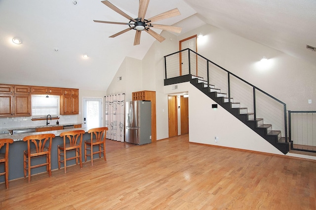 kitchen with stainless steel fridge, a breakfast bar area, brown cabinets, light wood-style floors, and a sink