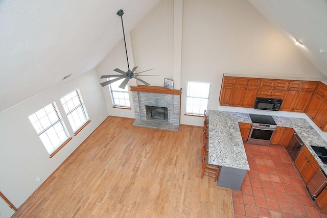 kitchen with black microwave, light stone counters, wall oven, open floor plan, and brown cabinets