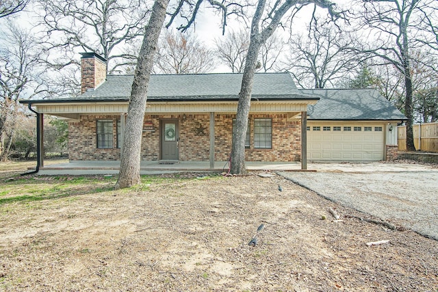 view of front facade with brick siding, a chimney, covered porch, an attached garage, and driveway