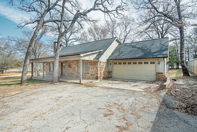 exterior space featuring aphalt driveway, roof with shingles, an attached garage, covered porch, and brick siding