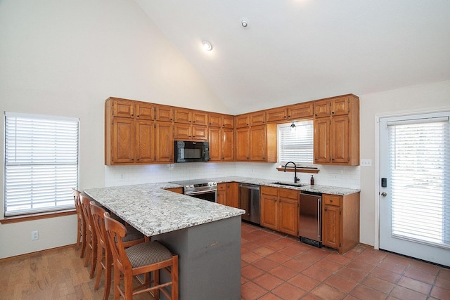 kitchen with a peninsula, a kitchen bar, appliances with stainless steel finishes, and brown cabinets