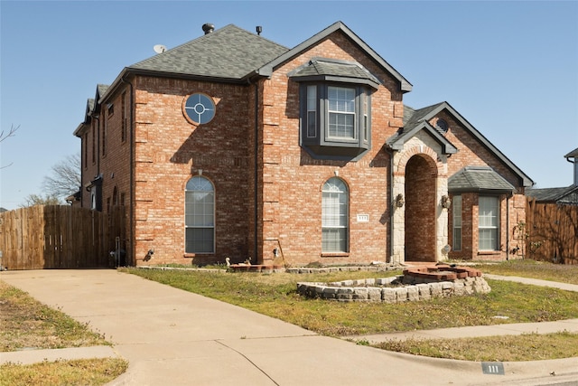 traditional home with a shingled roof, fence, and brick siding