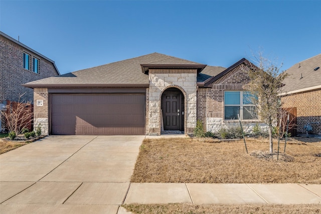 french country inspired facade featuring brick siding, a shingled roof, concrete driveway, an attached garage, and stone siding