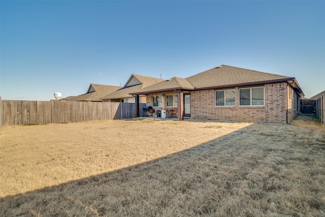 rear view of property with a shingled roof, a patio area, brick siding, and a fenced backyard