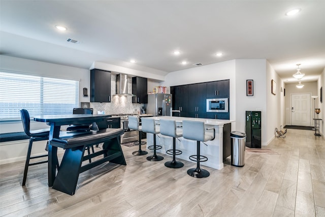 kitchen with stainless steel appliances, visible vents, light countertops, wall chimney range hood, and a kitchen bar