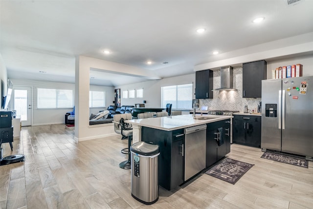 kitchen with wall chimney exhaust hood, open floor plan, stainless steel appliances, dark cabinetry, and light countertops