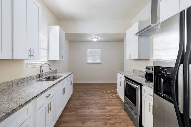 kitchen with light stone counters, a sink, white cabinetry, appliances with stainless steel finishes, and wall chimney exhaust hood