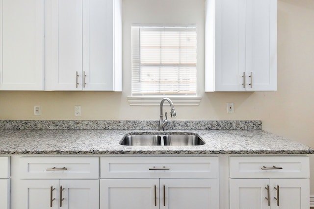 kitchen with white cabinetry, a sink, and light stone countertops