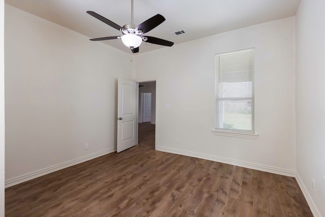 spare room featuring a ceiling fan, visible vents, dark wood finished floors, and baseboards