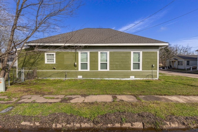 rear view of house featuring a shingled roof, fence, and a lawn