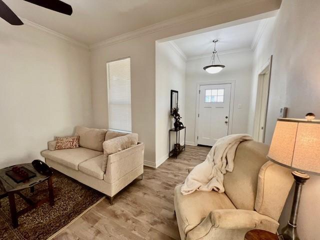 living area featuring a ceiling fan, light wood-style flooring, ornamental molding, and baseboards