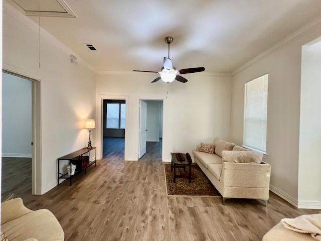 living room with crown molding, visible vents, attic access, wood finished floors, and baseboards