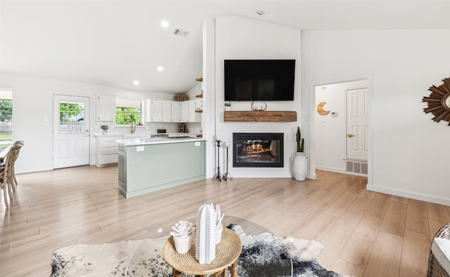 living room featuring vaulted ceiling, light wood finished floors, a glass covered fireplace, and visible vents