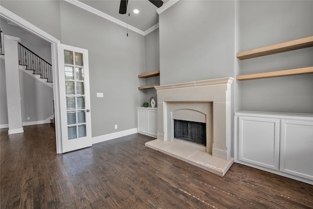 unfurnished living room with baseboards, a fireplace with raised hearth, ceiling fan, ornamental molding, and dark wood-style flooring