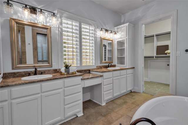 bathroom with a tub to relax in, a walk in closet, and vanity