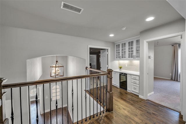 corridor with visible vents, arched walkways, dark wood-style floors, wine cooler, and a notable chandelier