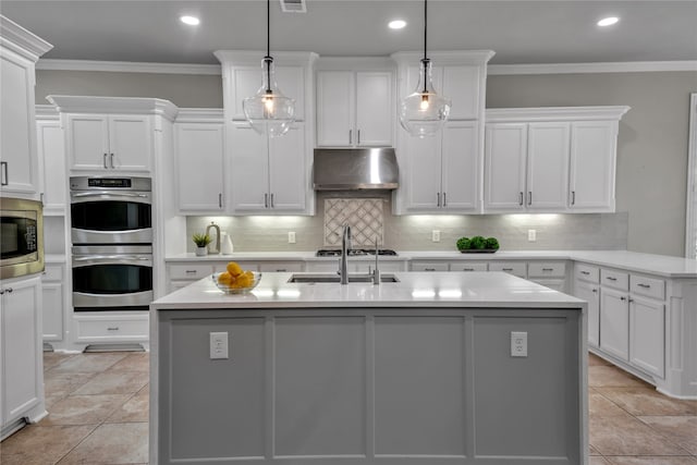 kitchen featuring decorative light fixtures, a kitchen island with sink, light countertops, and under cabinet range hood