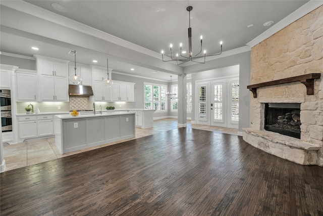 kitchen with under cabinet range hood, open floor plan, light countertops, an island with sink, and pendant lighting