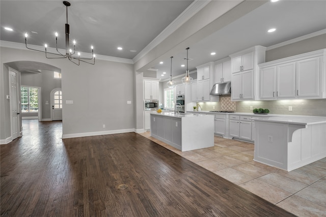 kitchen featuring light countertops, stainless steel microwave, white cabinetry, and under cabinet range hood