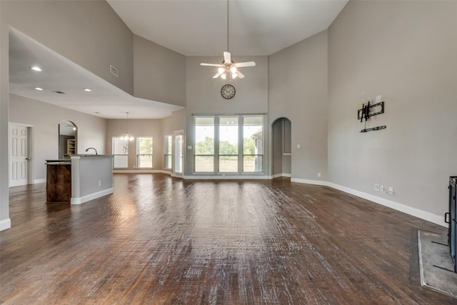 unfurnished living room with baseboards, arched walkways, dark wood-type flooring, and ceiling fan with notable chandelier