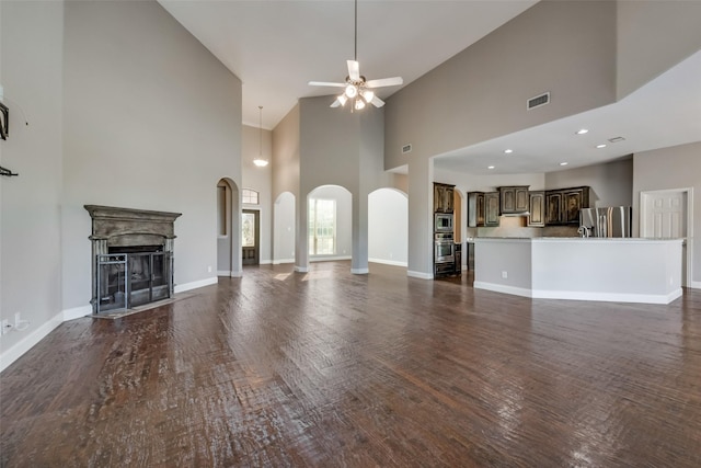 unfurnished living room with arched walkways, visible vents, dark wood-type flooring, a high end fireplace, and a ceiling fan