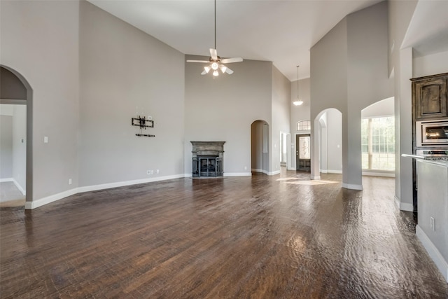 unfurnished living room featuring ceiling fan, a fireplace, arched walkways, and dark wood-style flooring