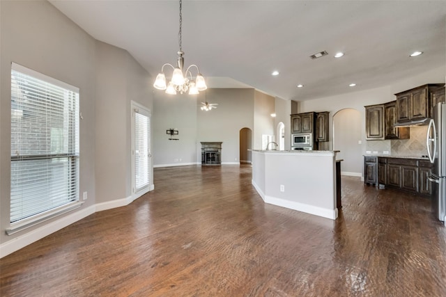 kitchen with arched walkways, dark wood-style floors, decorative light fixtures, a kitchen island with sink, and stainless steel appliances