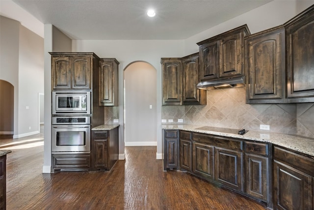 kitchen featuring dark brown cabinetry, under cabinet range hood, appliances with stainless steel finishes, and arched walkways