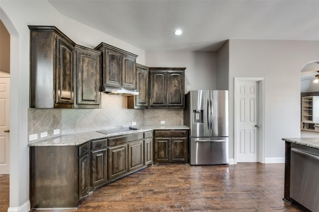 kitchen featuring arched walkways, dark wood-style flooring, appliances with stainless steel finishes, dark brown cabinets, and light stone countertops