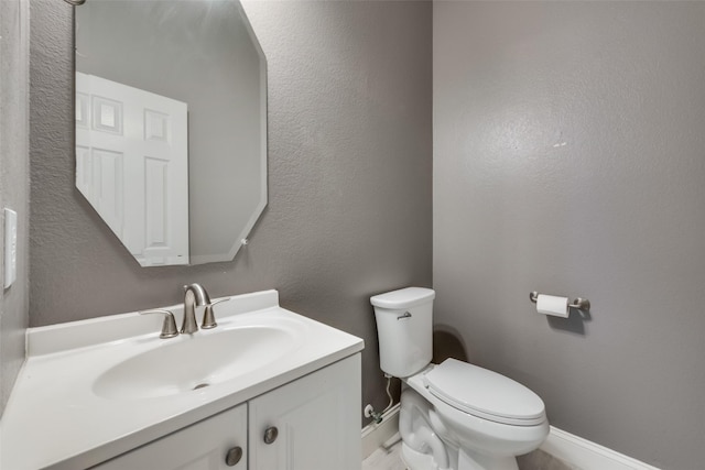 bathroom with toilet, a textured wall, baseboards, and vanity