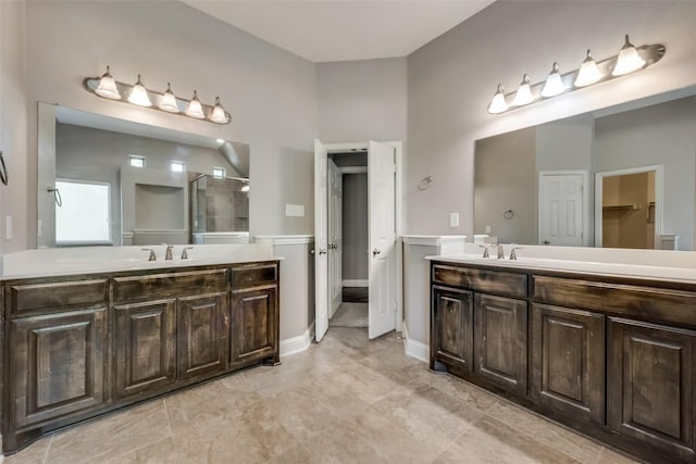 bathroom with a stall shower, two vanities, a sink, and baseboards