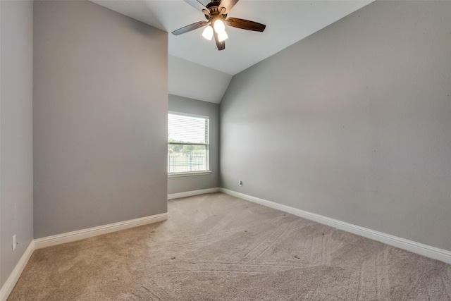 spare room featuring a ceiling fan, light colored carpet, vaulted ceiling, and baseboards