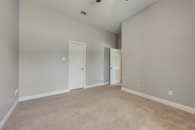 spare room with ceiling fan, light colored carpet, a high ceiling, visible vents, and baseboards