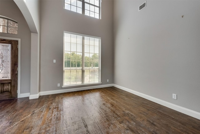 entrance foyer featuring baseboards, visible vents, arched walkways, a towering ceiling, and dark wood-style floors