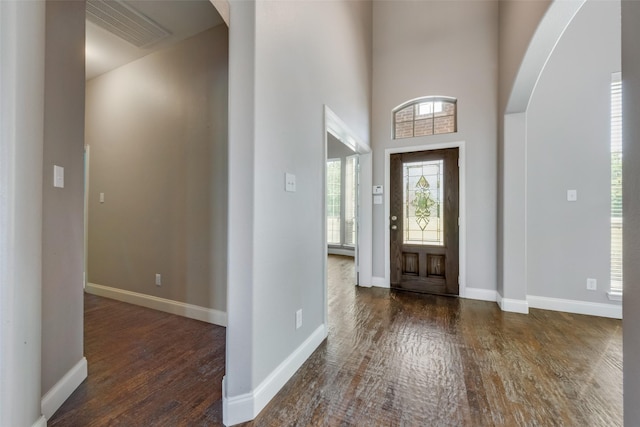 entryway with arched walkways, dark wood-style flooring, visible vents, and baseboards